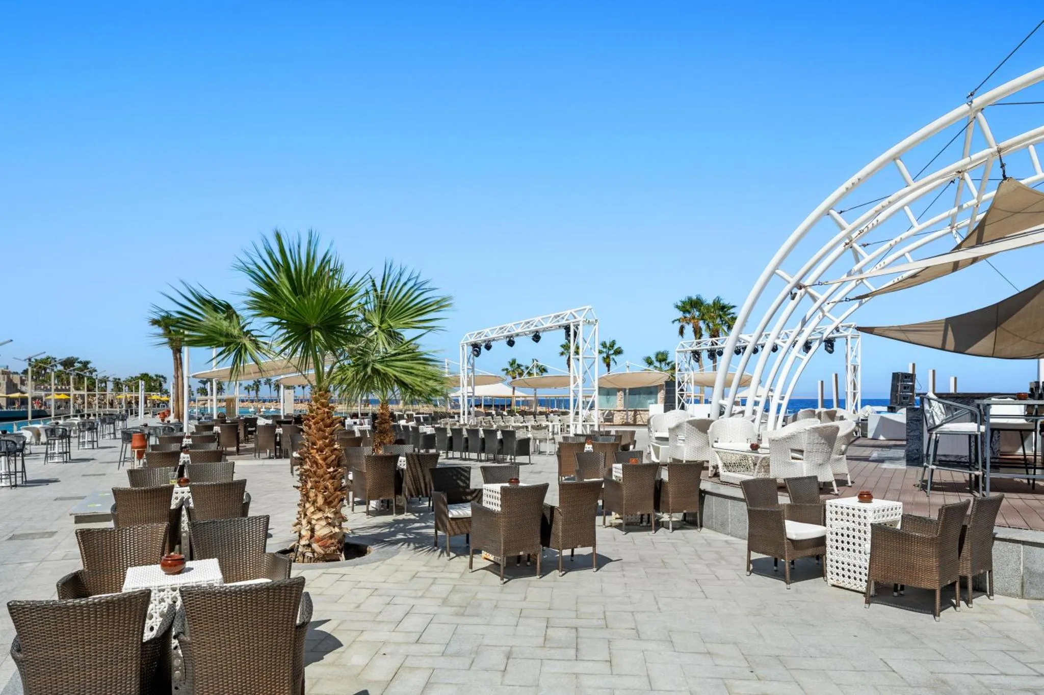 Terrasse ombragée avec tables et chaises en osier face à la mer.