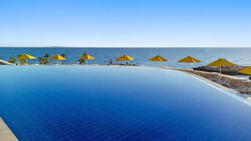 Une piscine bleue à débordement avec des parasols jaunes et des transats.