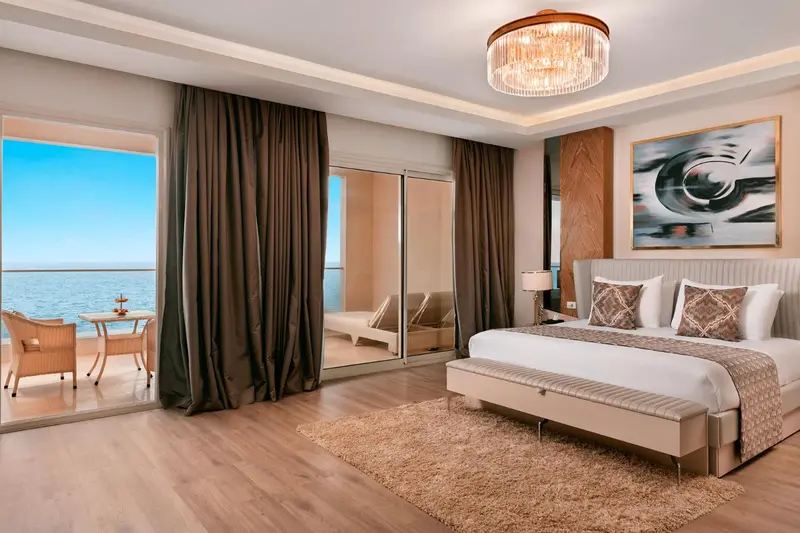 Chambre lumineuse avec un grand lit et une vue sur la mer depuis un balcon.