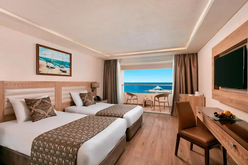 Chambre lumineuse avec deux lits et vue sur la mer.