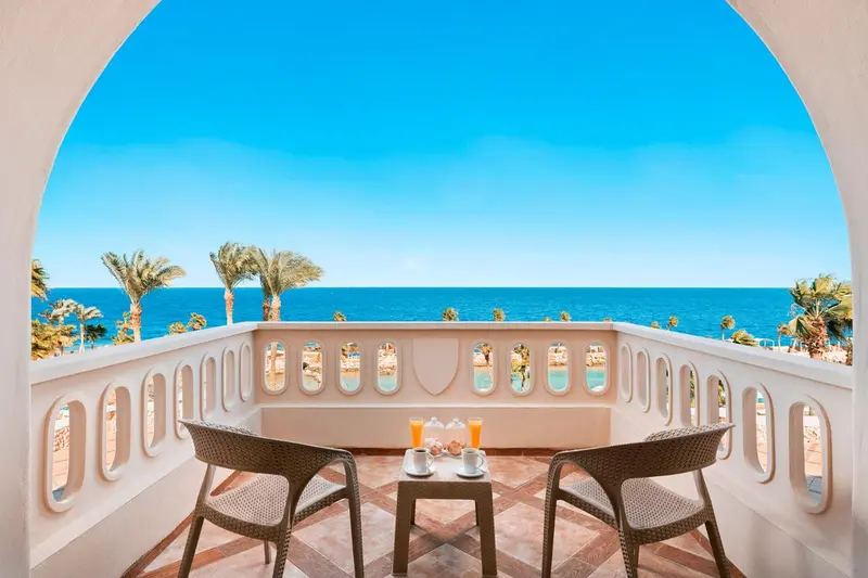 Deux fauteuils et une table basse sur un balcon avec vue sur la mer.