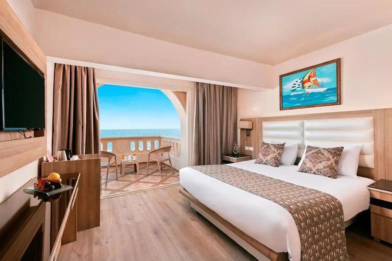 Chambre lumineuse avec un grand lit et une vue sur la mer depuis un balcon.