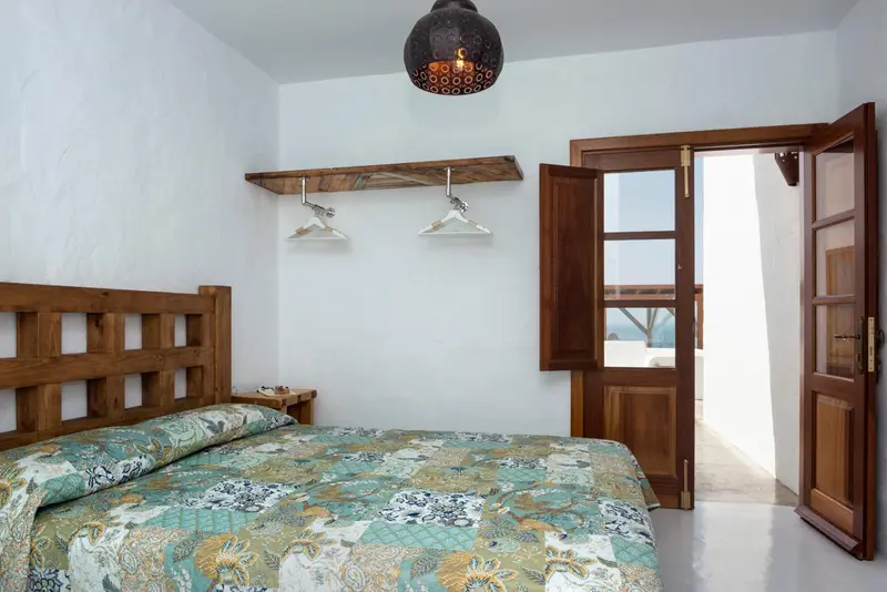 Une chambre lumineuse avec un lit recouvert d'une courtepointe colorée et une porte ouverte sur une terrasse.