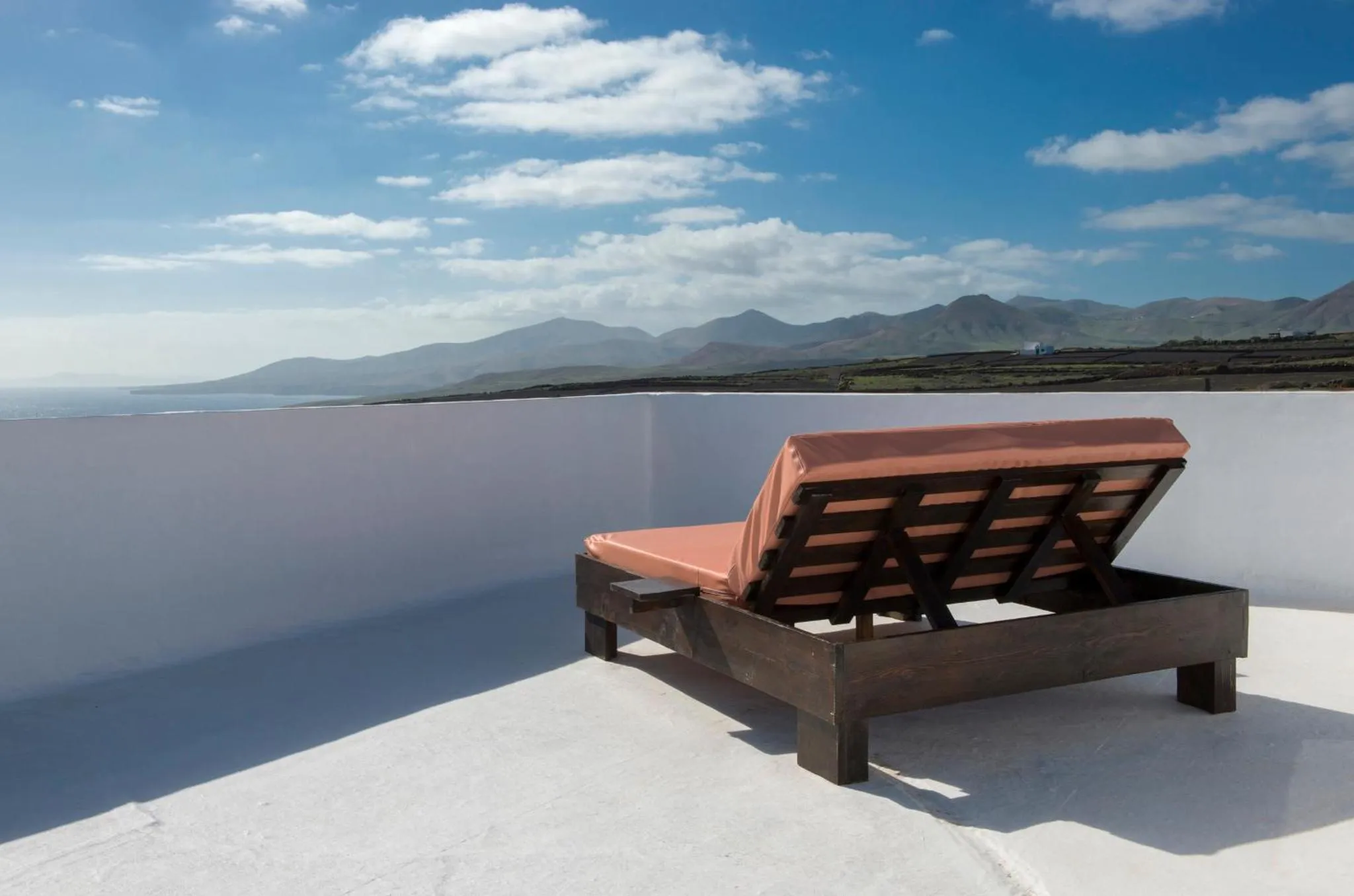 Deux transats en bois sur une terrasse blanche avec vue sur la mer et les montagnes.