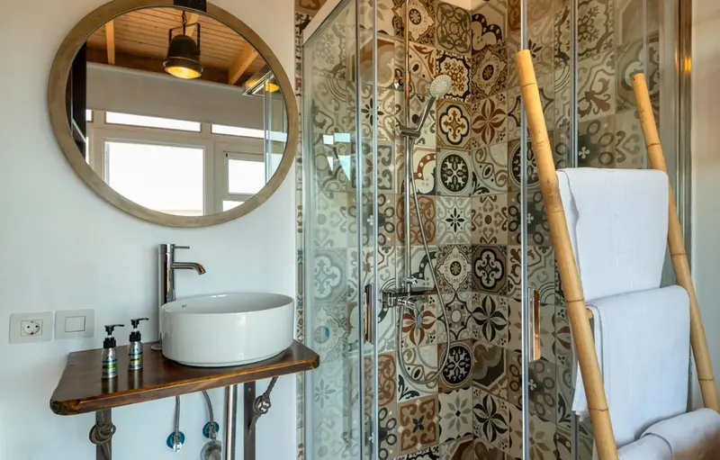 Une salle de bain lumineuse avec une douche à l'italienne décorée de motifs colorés et un lavabo sur console en bois.