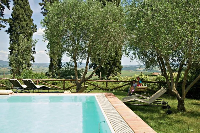 Des transats sont disposés au bord d'une piscine dans un jardin arboré.