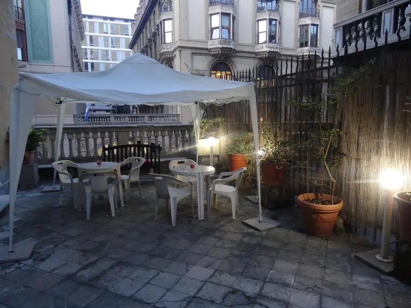 Une terrasse pavée avec des tables et des chaises en plastique blanc sous un auvent.