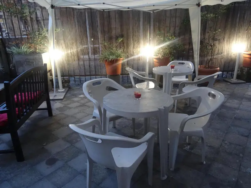 Tables et chaises en plastique sur une terrasse pavée éclairée de lampes.
