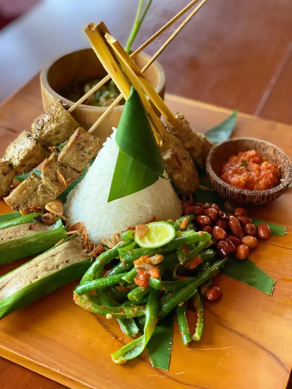 Assiette de plats traditionnels indonésiens avec du riz, du tofu, des haricots verts et une sauce épicée.