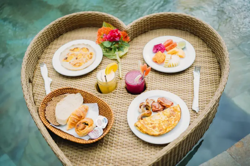 Un plateau de petit-déjeuner en forme de cœur flotte sur une piscine.