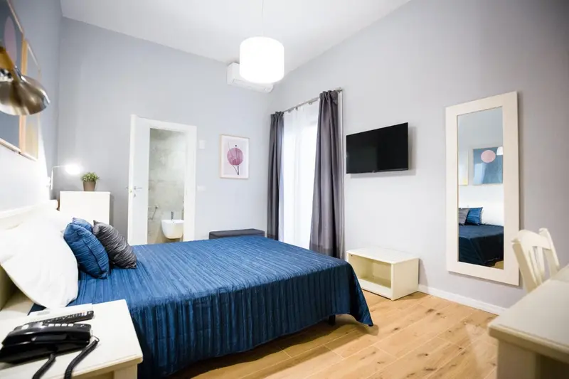 Une chambre lumineuse avec un grand lit recouvert d'une couette bleue et de coussins.