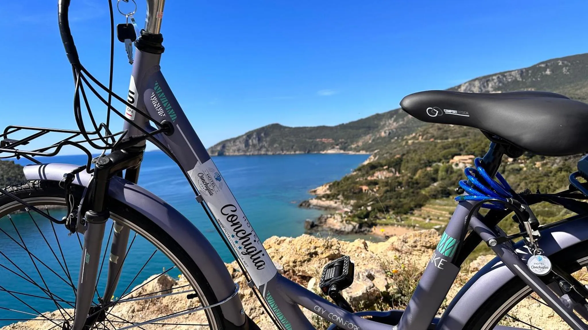 Un vélo gris est garé sur une colline surplombant la mer et le paysage côtier.