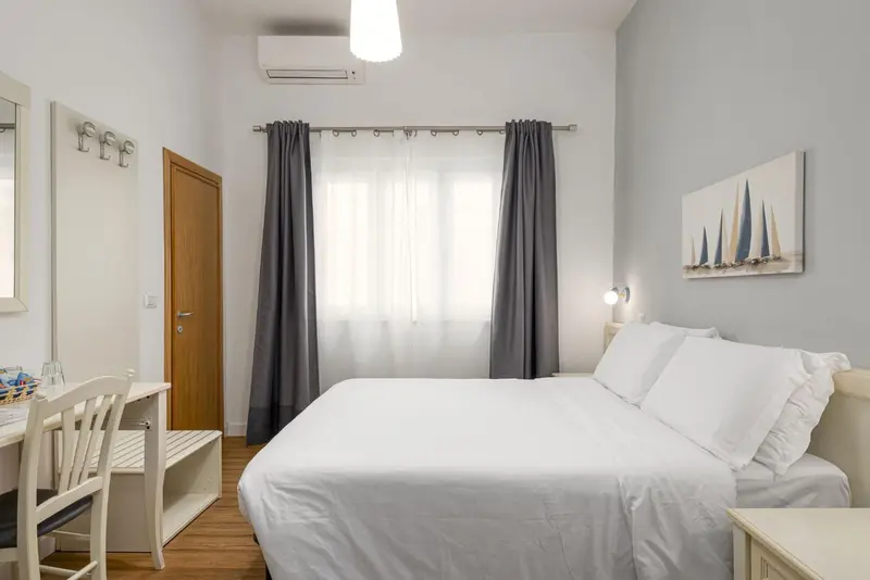 Une chambre lumineuse avec un lit blanc et un bureau.