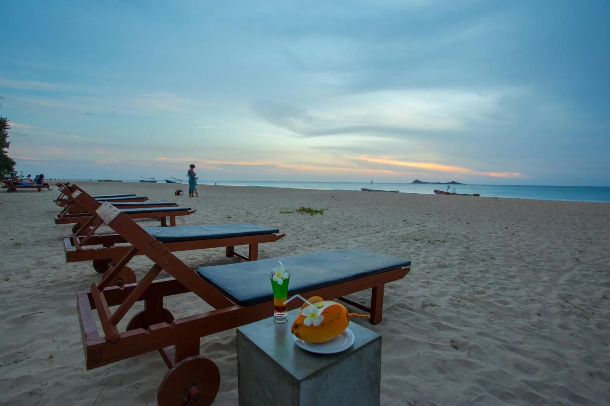 Transats alignés sur une plage de sable fin au coucher du soleil.