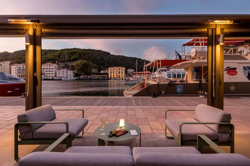 Terrasse avec mobilier d'extérieur donnant sur un port au coucher du soleil.