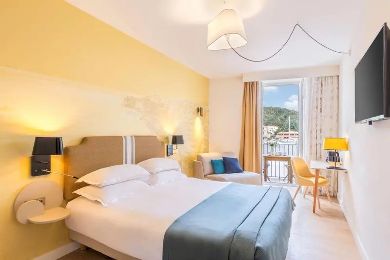 Chambre lumineuse avec un lit double et un coin salon donnant sur un balcon.