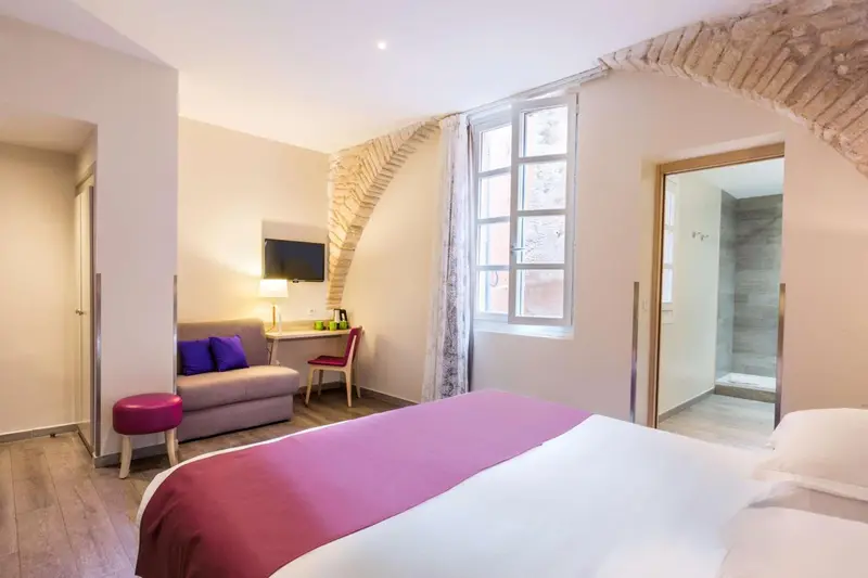 Une chambre lumineuse avec un lit recouvert d'une couverture colorée et un canapé.
