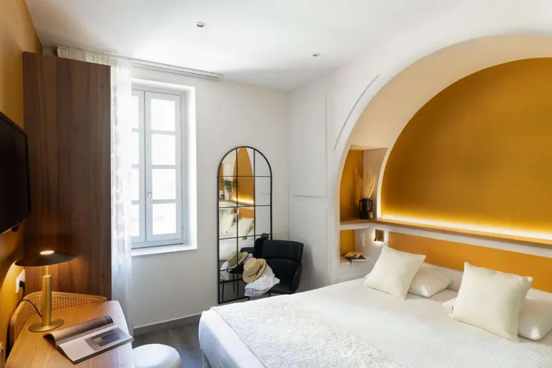 Une chambre lumineuse avec un lit blanc et un mur jaune.
