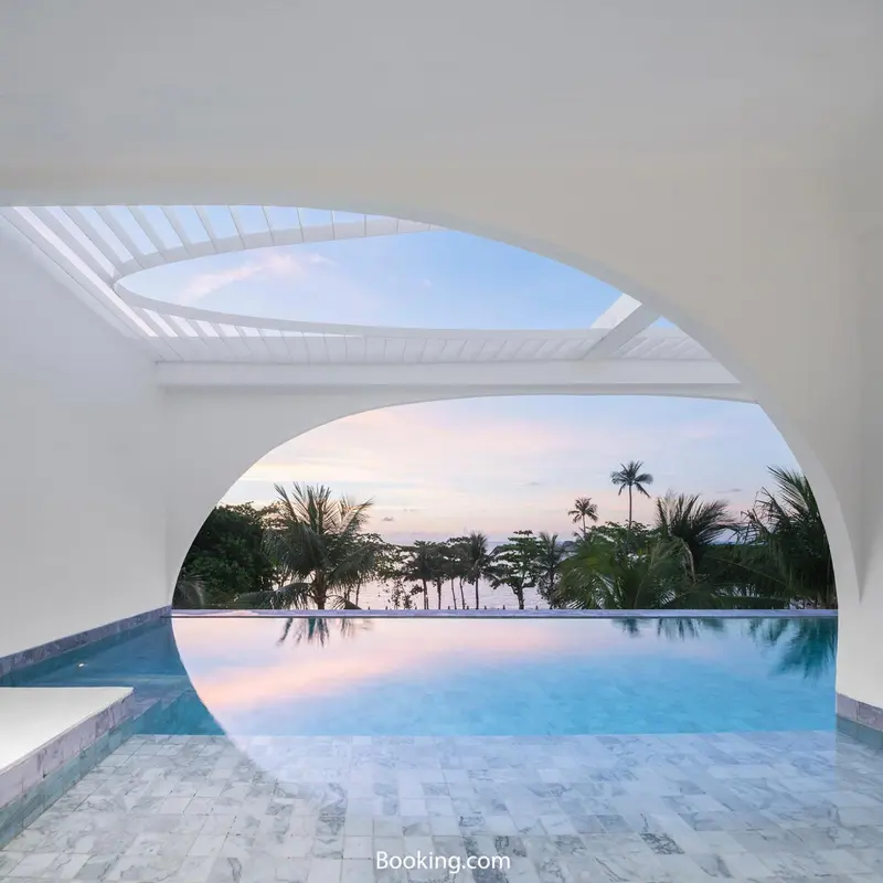 Une piscine à débordement reflète le ciel crépusculaire et la végétation tropicale.