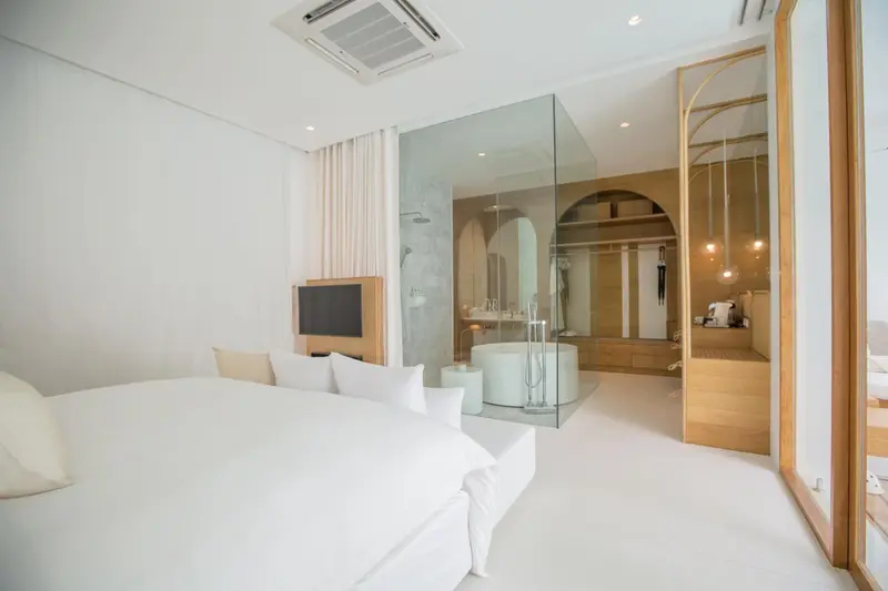 Chambre lumineuse avec un grand lit et une salle de bain ouverte.