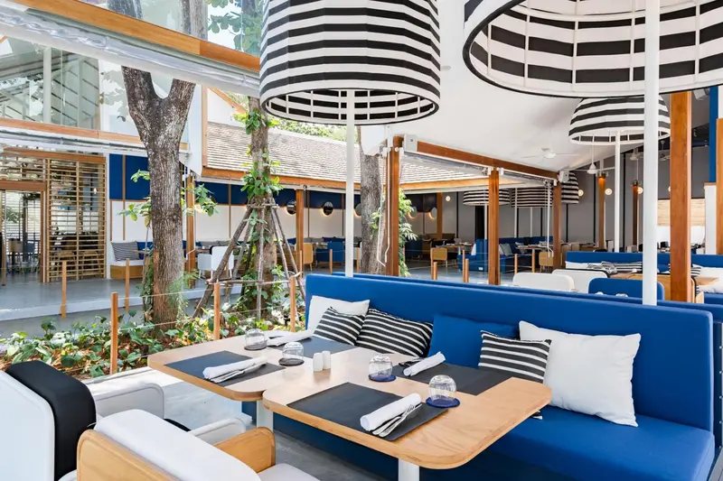 Une salle à manger lumineuse avec des tables dressées et des banquettes bleues.