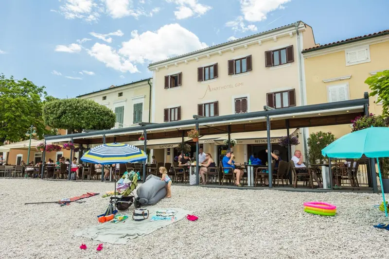 Terrasse ombragée avec tables et chaises devant un bâtiment clair.