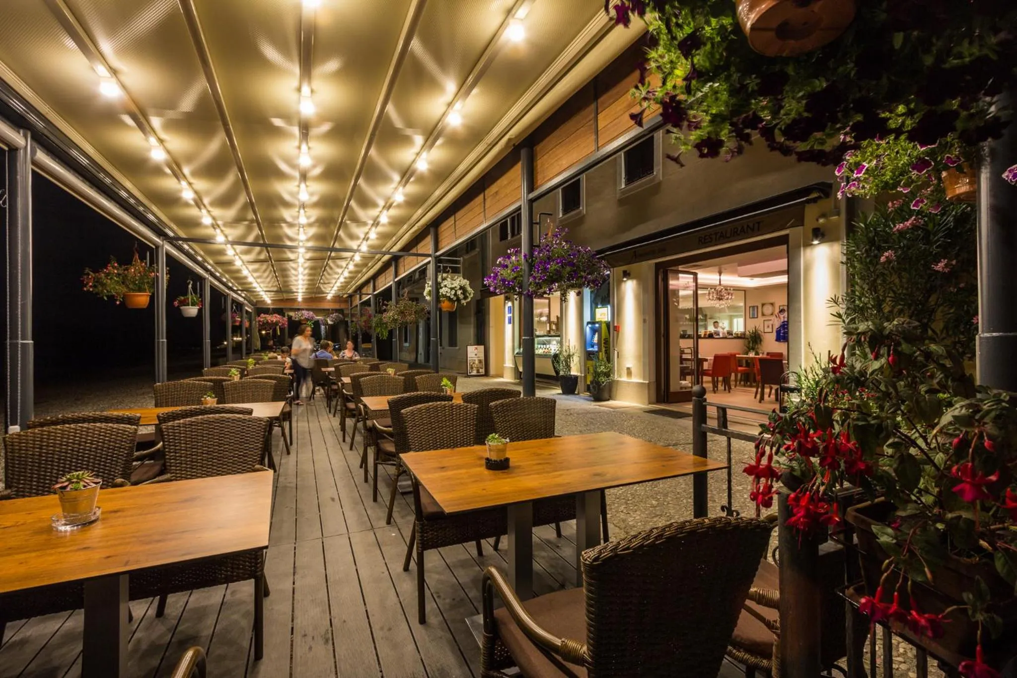 Terrasse lumineuse avec tables et chaises en bois, décorée de plantes fleuries.