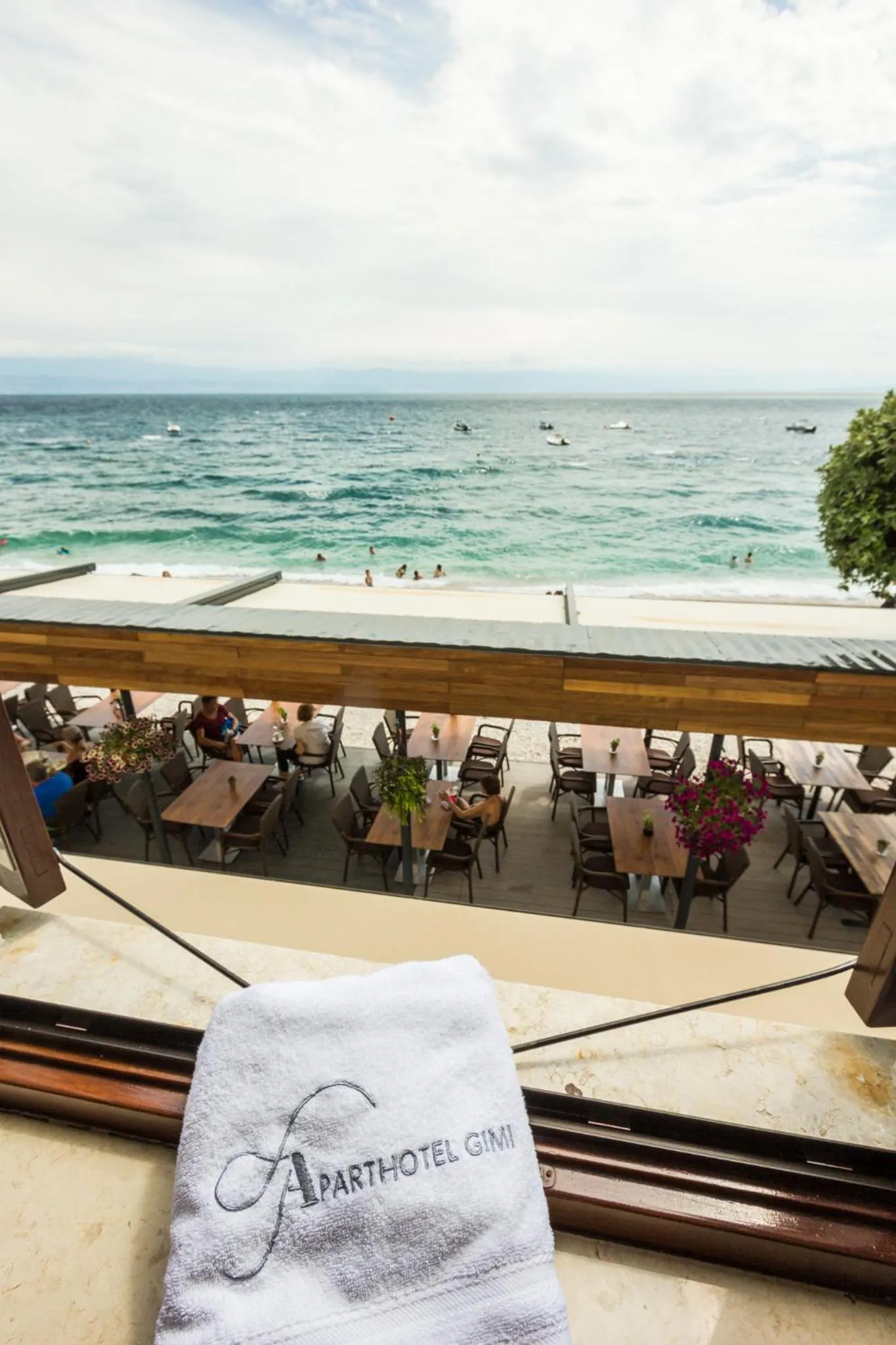 Terrasse ombragée avec tables et chaises donnant sur la mer et la plage.