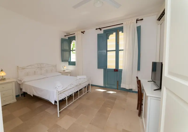 Une chambre lumineuse avec un lit blanc et des fenêtres bleues.