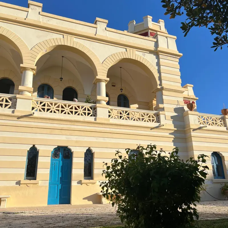Bâtiment blanc à deux étages avec des arches et un balcon orné.