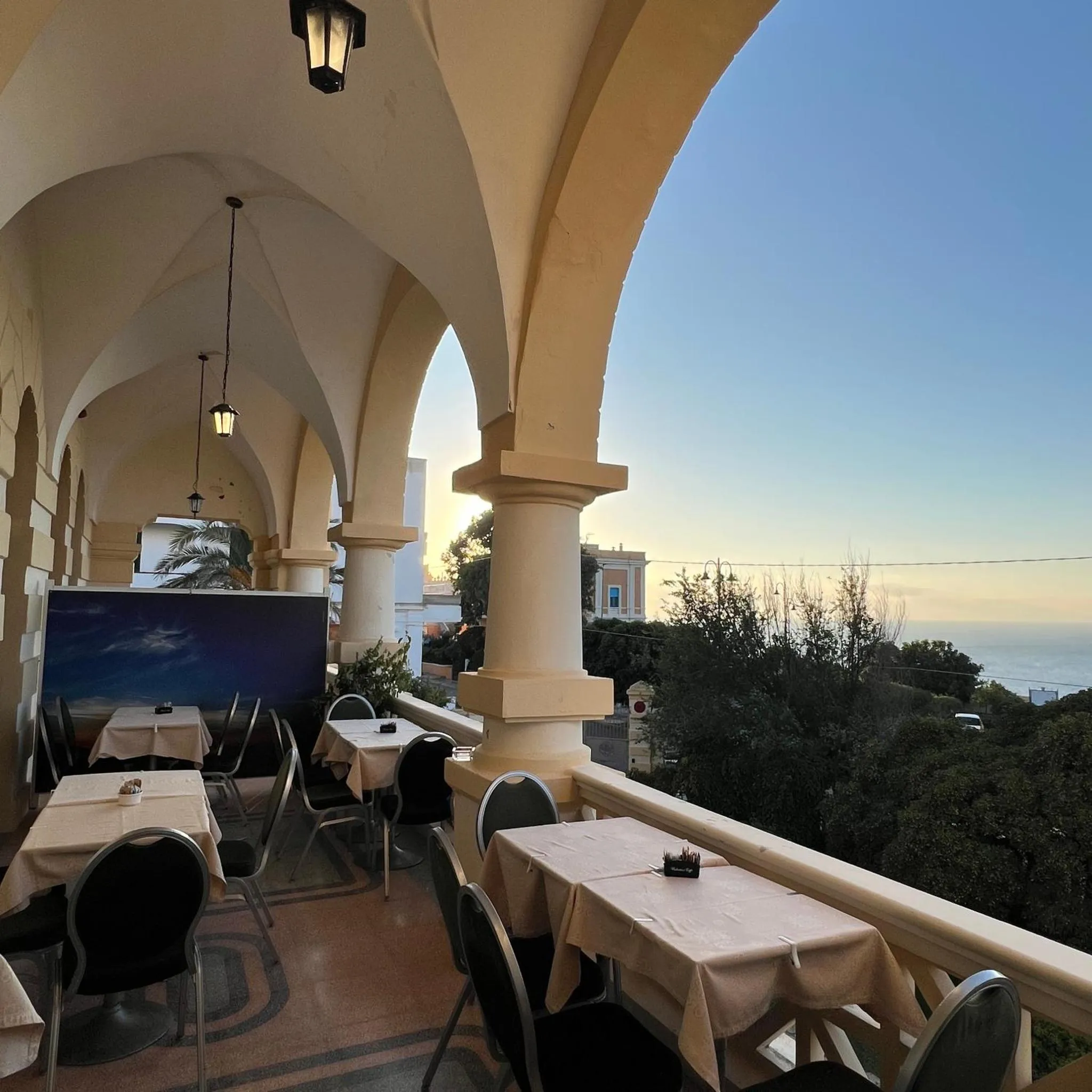 Terrasse ombragée avec tables et chaises donnant sur la mer.