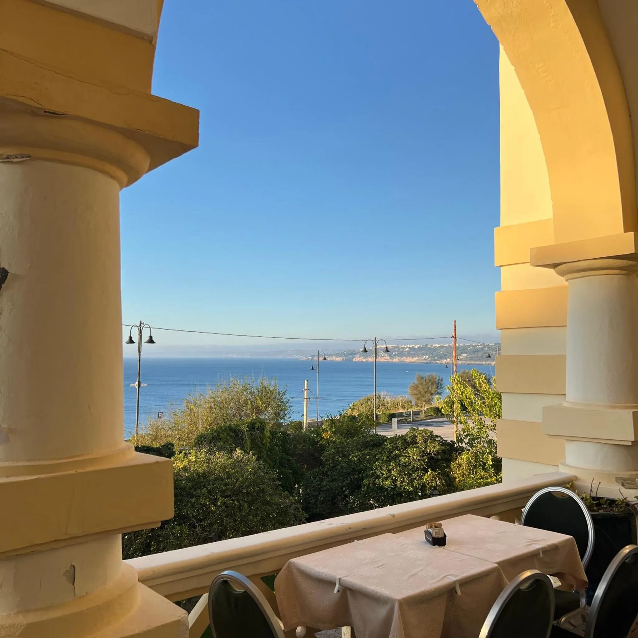 Vue sur la mer depuis une terrasse ombragée avec une table dressée.