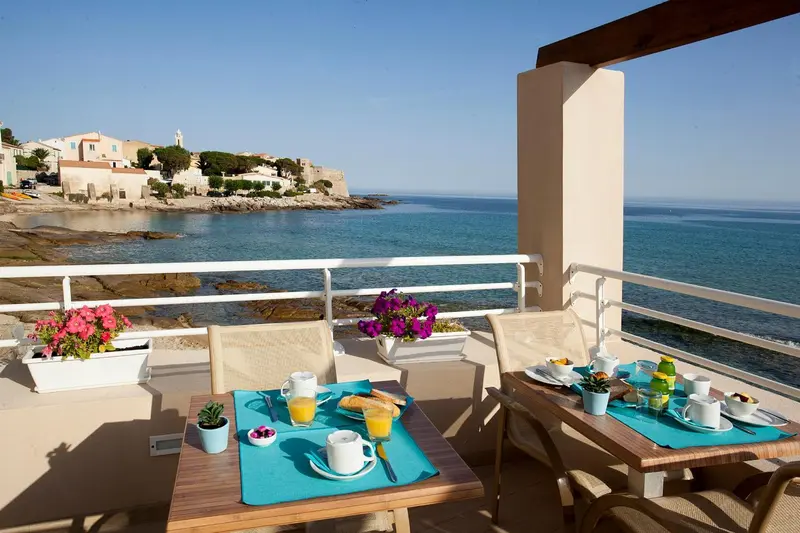 Une terrasse ensoleillée offre une vue sur la mer et un village côtier.