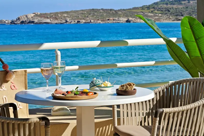 Une table est dressée avec des plats et des boissons sur une terrasse en bord de mer.
