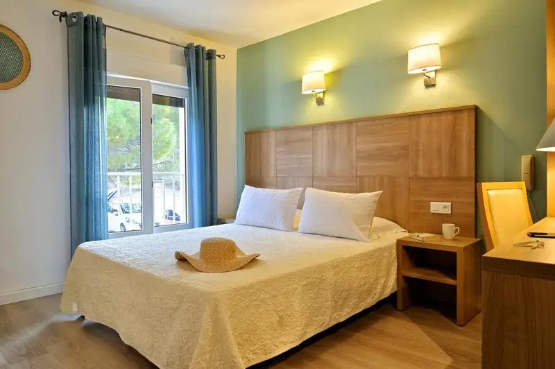 Une chambre lumineuse avec un grand lit recouvert d'une courtepointe blanche et d'un chapeau de paille.