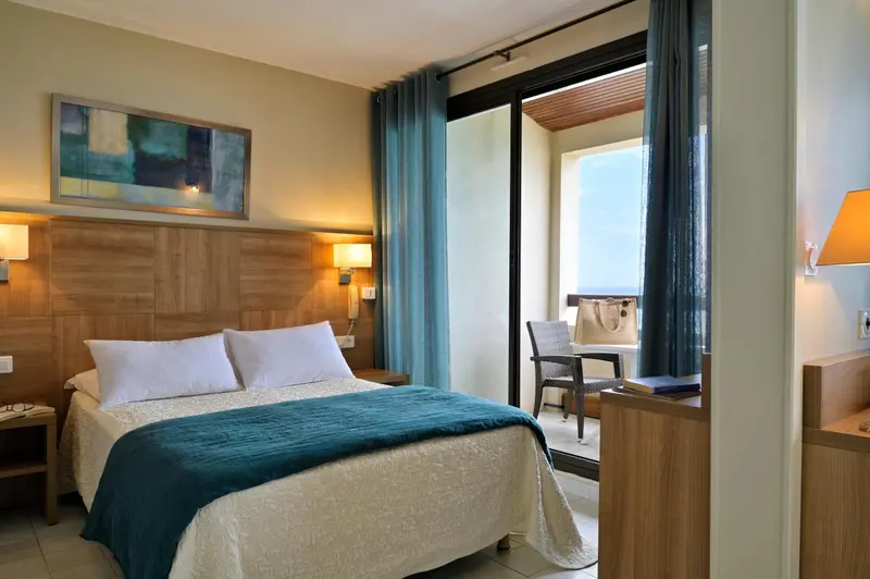Une chambre lumineuse avec un lit recouvert d'une couverture turquoise et un balcon.