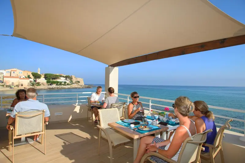 Des convives prennent leur repas sur une terrasse ensoleillée avec vue sur la mer.