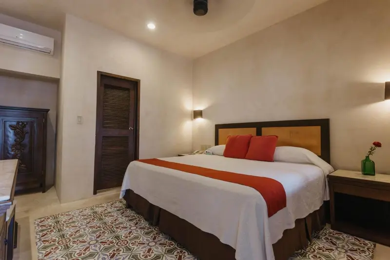 Une chambre lumineuse avec un grand lit recouvert d'une courtepointe rouge et de coussins.