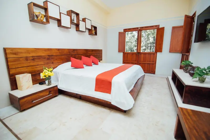 Une chambre lumineuse avec un grand lit recouvert d'une courtepointe rouge et de coussins.