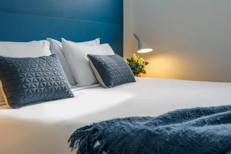 Un lit avec des oreillers et une couverture est mis en valeur par un éclairage doux.