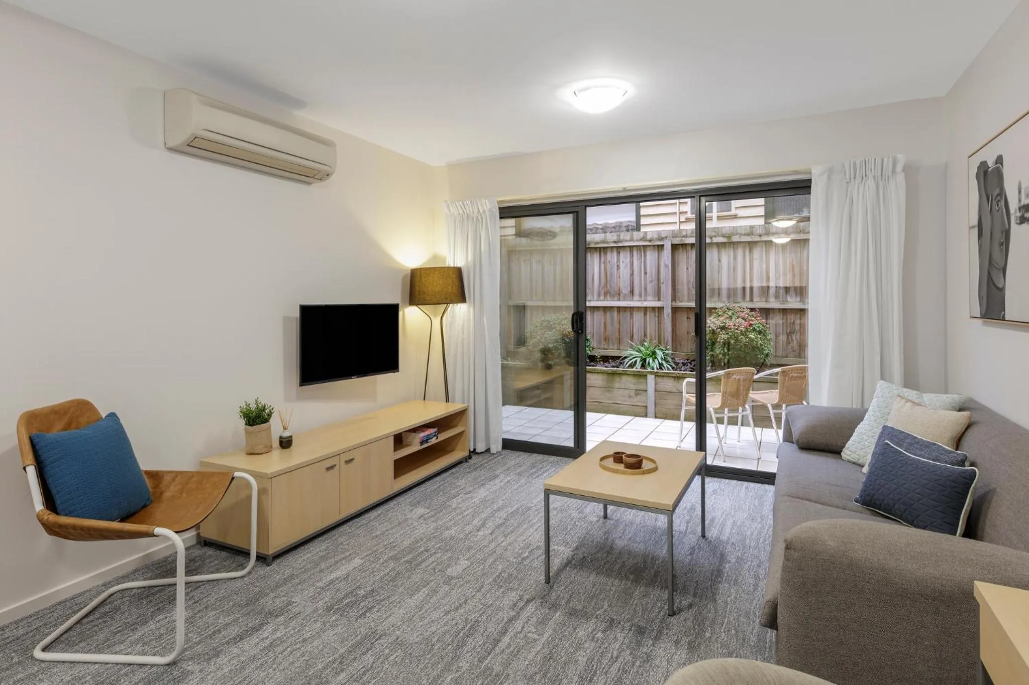 Un salon lumineux avec canapés et fauteuil face à un téléviseur et une porte-fenêtre donnant sur une terrasse.