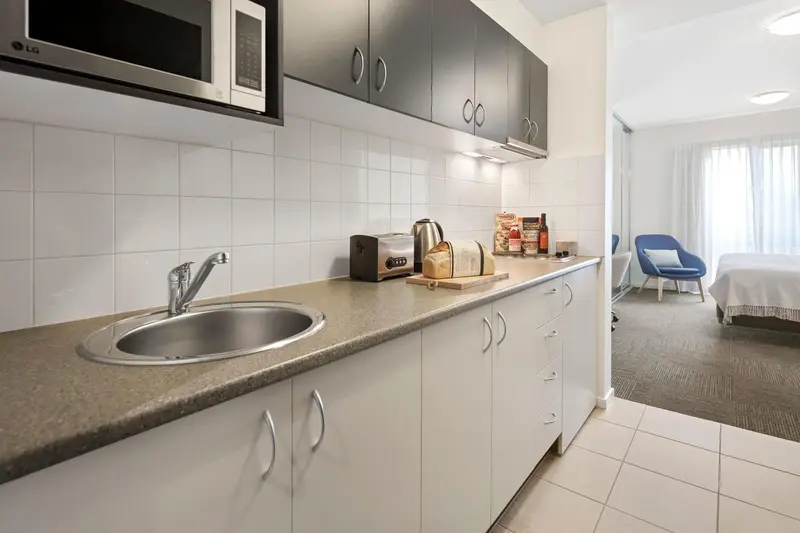 Une kitchenette lumineuse avec un évier, des placards et un plan de travail.