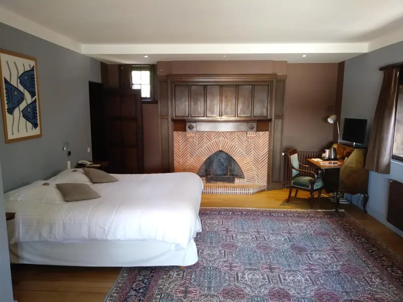 Une chambre lumineuse avec un grand lit et une cheminée en briques.