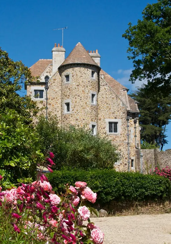 Bâtiment en pierre avec tourelles et végétation fleurie en premier plan.