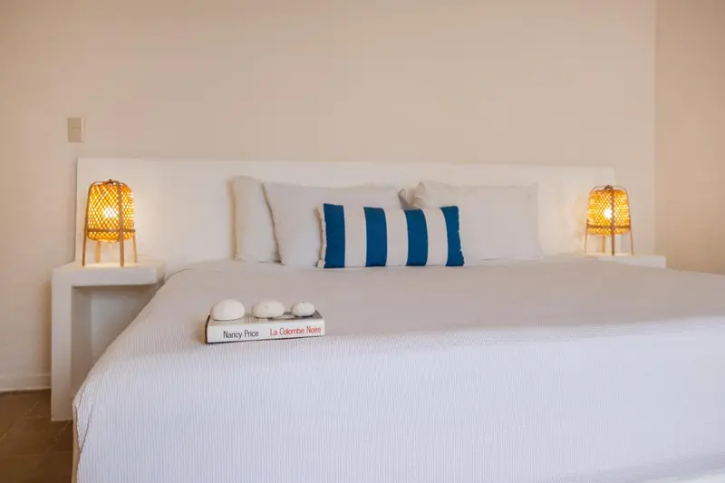 Un lit blanc avec des oreillers bleus et des lampes de chevet en rotin.