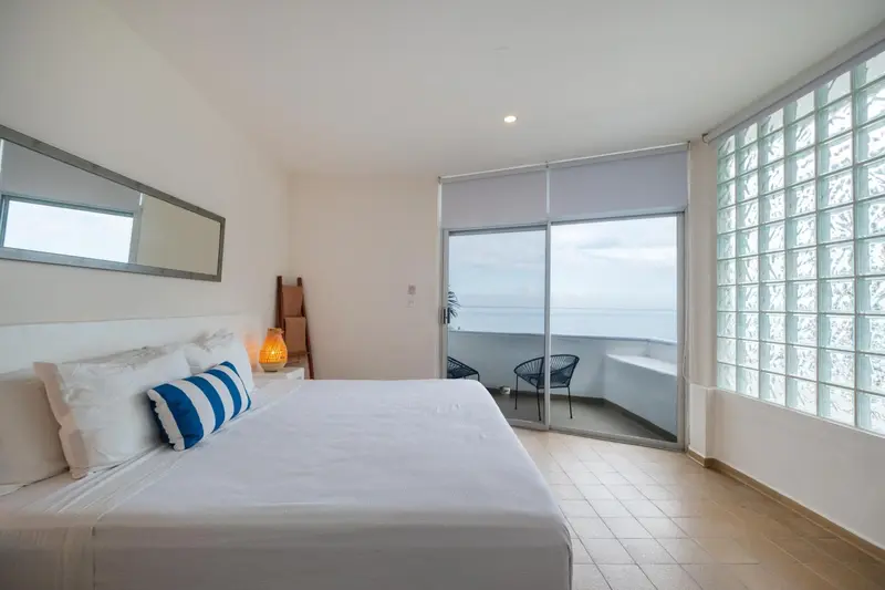 Une chambre lumineuse avec un grand lit face à une baie vitrée donnant sur la mer.