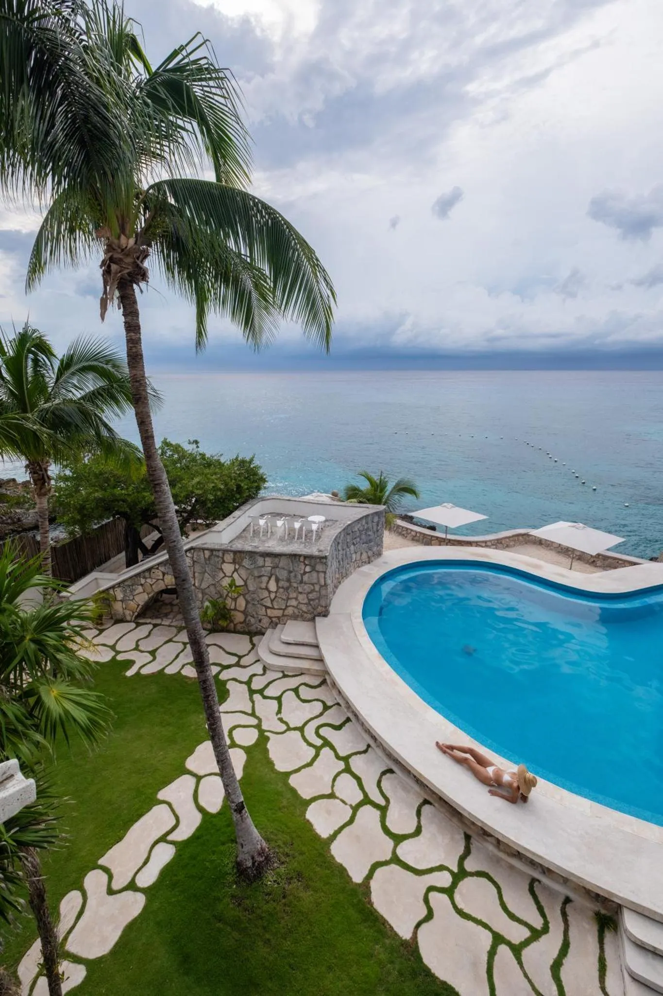 Une piscine turquoise bordée d'une terrasse en pierre, avec une vue sur la mer.