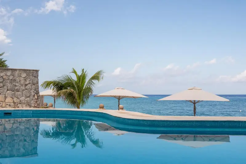 Une piscine à débordement surplombe la mer turquoise sous un ciel bleu.
