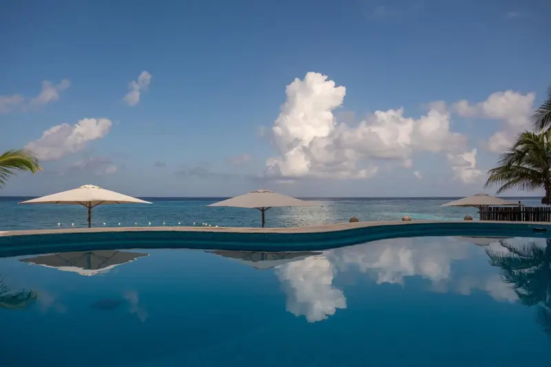 Piscine à débordement avec parasols et vue sur la mer.