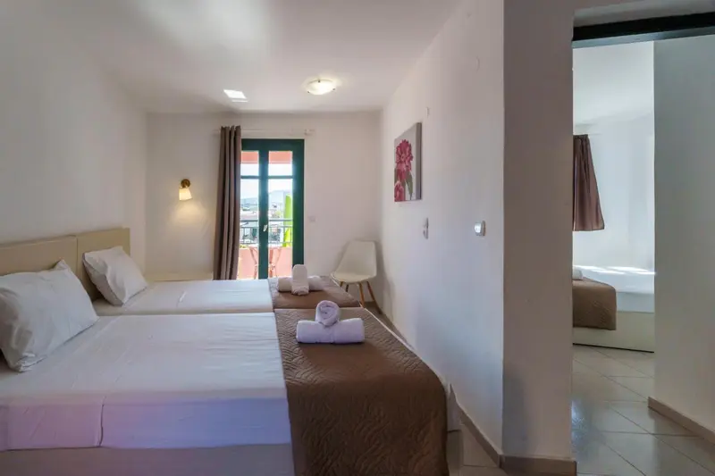 Chambre lumineuse avec deux lits simples et une porte-fenêtre donnant sur l'extérieur.